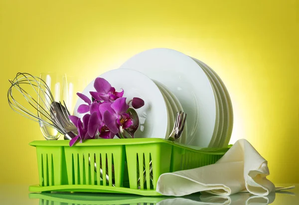 Washed dishes and utensils in the green dryer on yellow background, an orchid branch and dishwashing