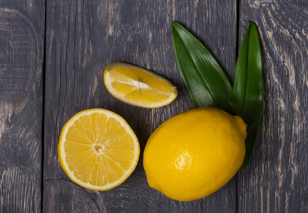 Jugoso limón y piezas decoradas con hojas en tablas de madera oscura — Foto de Stock