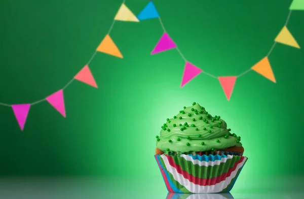 Feestelijke cupcake met crème op groene achtergrond versierd met kleurrijke slinger — Stockfoto