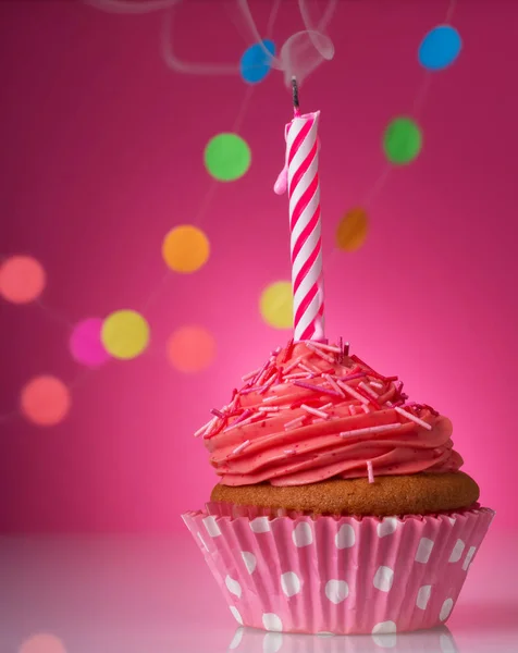 Festive cupcake with candle and cream on pink background decorated with colorful confetti — Stock Photo, Image