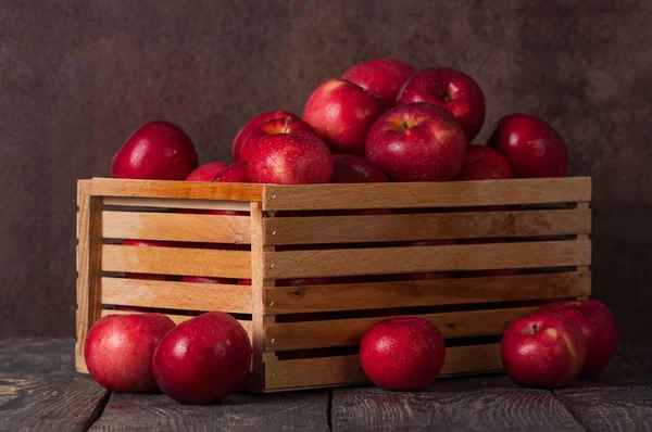 Wooden box full of apples in drops of water on dark — Stock Photo, Image