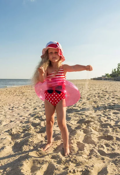 Lyse pige i en gummiring og leger med sand på solrig strand - Stock-foto