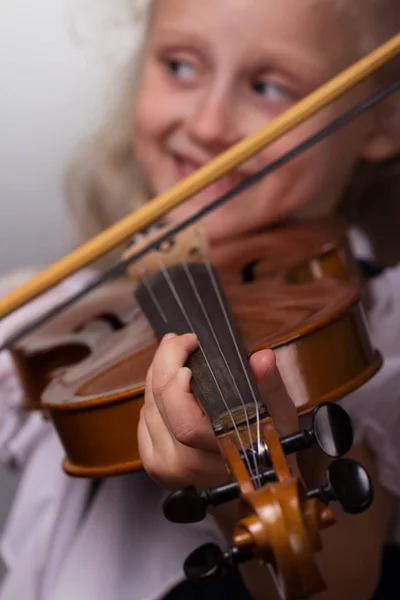 Милая маленькая девочка в яркой блузке играет на скрипке крупным планом на сером фоне — стоковое фото