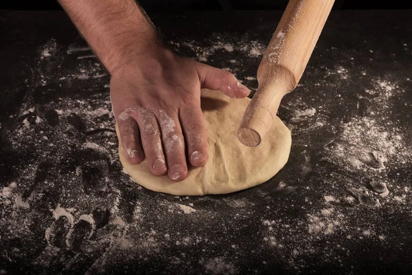 Male hands of the chef rolled out the pizza dough on dark table — Stock Photo, Image