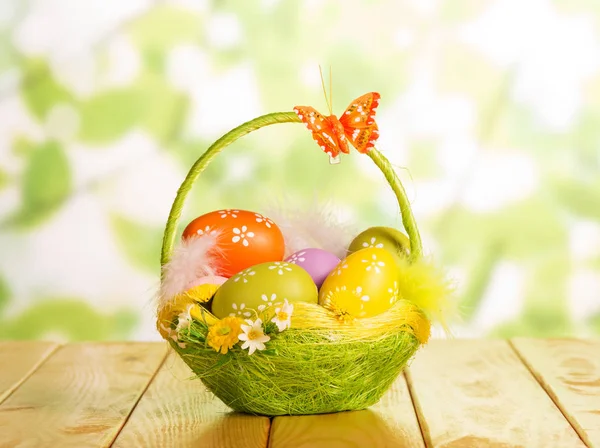 Huevos de Pascua en cesta, plumas y mariposa en verde abstracto . —  Fotos de Stock