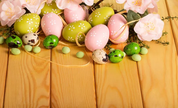 Varie uova di Pasqua, erba, fiori, caramelle, nastro su legno chiaro . — Foto Stock