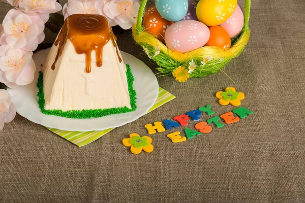 Easter eggs, cheesecake dessert, inscription Happy Easter and flowers on sackcloth. — Stock Photo, Image