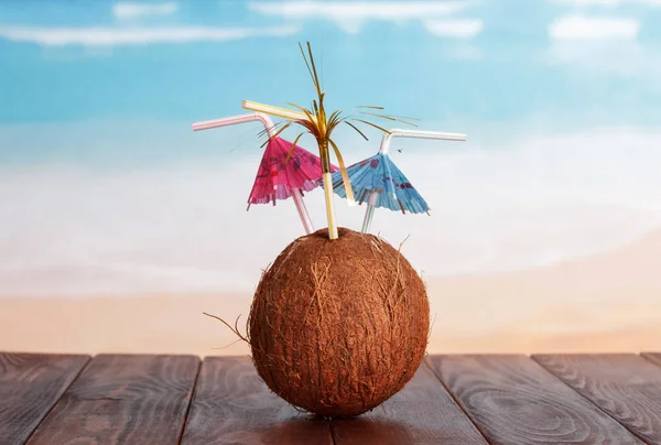 Кокос с соломинками и зонтиками на столе у моря . — стоковое фото