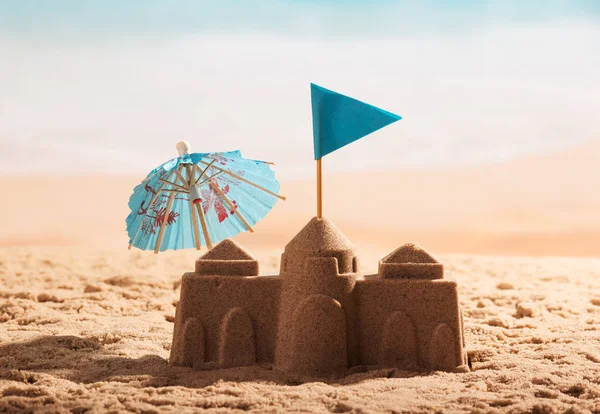 Palacio de arena, bandera azul y paraguas en la costa . — Foto de Stock