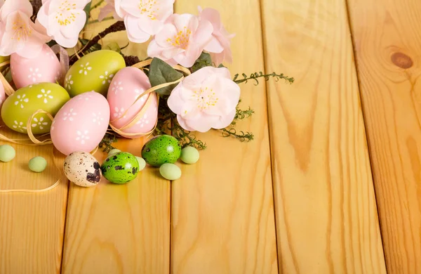 Ostereier, Gras, Blumen, Süßigkeiten auf hellem Holz. — Stockfoto