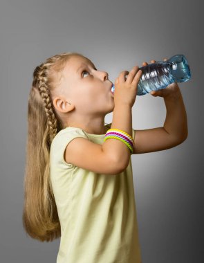 Uzun saçlı küçük bir kız, gri şişeden su içiyor.