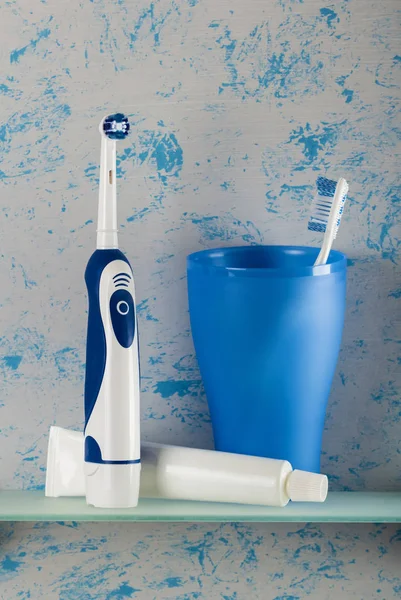 Electric toothbrush, toothpaste, manual brush in glass on shelf — 스톡 사진