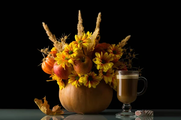 Ein Strauß Äpfel und Blumen in einem Kürbis, ein Glas Cappuccino und Süßigkeiten, isoliert auf schwarz — Stockfoto
