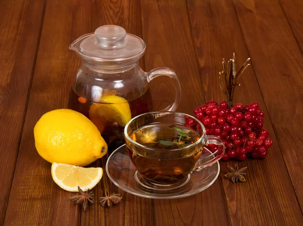 Pitcher van hete thee en citroen, kopje en schotel, bos viburnum bessen, op de achtergrond tafel — Stockfoto