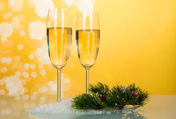 黄色の背景に人工雪の上にコーンとワインの2つのグラス、松の枝 — ストック写真