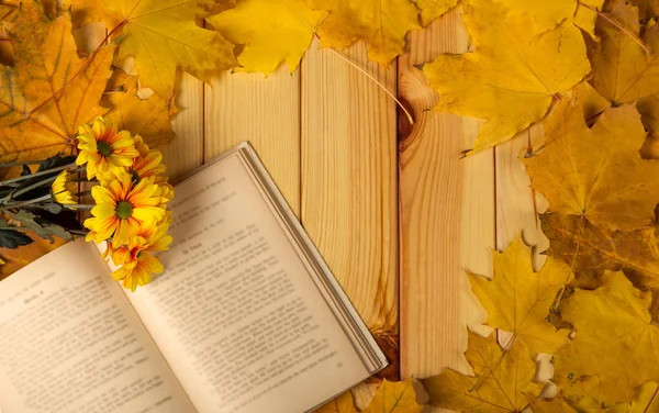 Egy nyitott könyv és egy kis csokor krizantém, őszi levelek az asztalon — Stock Fotó