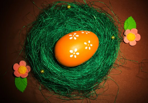 Gniazdo, pokryte trawą z jajkami wielkanocnymi i kwiatami na brązie. — Zdjęcie stockowe