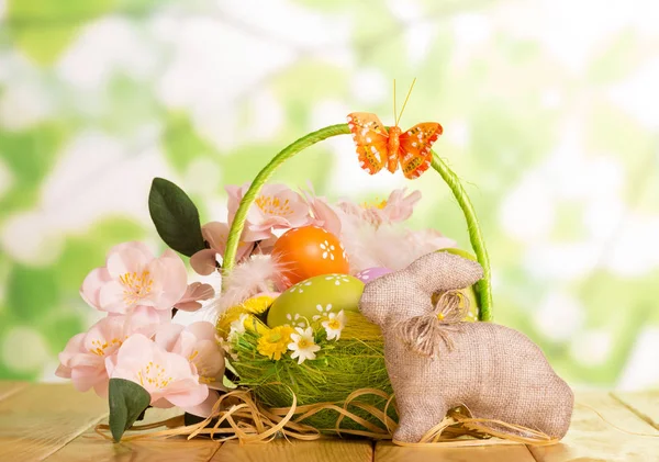 Ostereier im Korb, Hase und Blumen auf abstraktem Grün. — Stockfoto