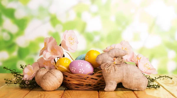 Uova di Pasqua in cesto e vicino, Coniglietto, ramo con fiori . — Foto Stock