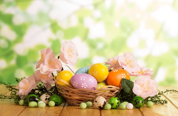 Kleurrijke paaseieren in mand en in de buurt, snoep, gras, bloemen. — Stockfoto