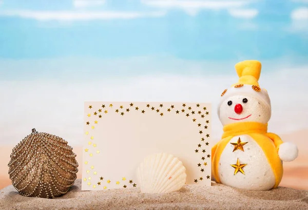 Snowman, blank card, Christmas ball, seashell in the sand — Stock Photo, Image