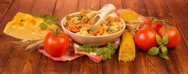 A bowl with farfalle and wooden scoop, bunch of spaghetti — Stock Photo, Image
