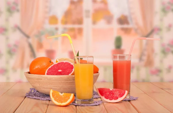 A bowl of citrus fruit, glasses of orange and grapefruit juices — Stock Photo, Image