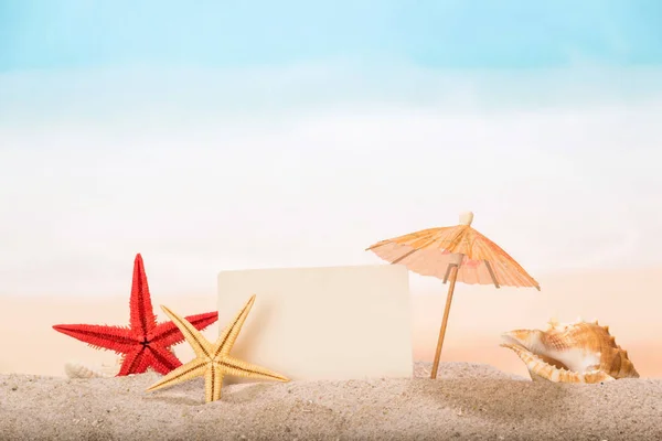 Tarjeta en blanco, estrellas de mar, paraguas y concha de mar de cerca en el san — Foto de Stock