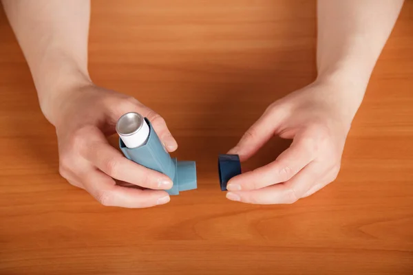 Vrouwelijke handen met inhalator aerosol op de achtergrond van de tafel. — Stockfoto