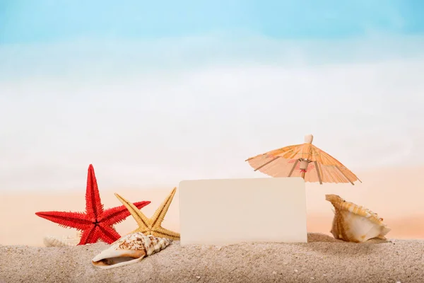 Una tarjeta en blanco, estrellas de mar, paraguas y conchas de mar en la arena —  Fotos de Stock