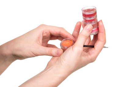 Kadın ellerinde, dudak parlatıcılı kavanozlar ve beyaz sırt fırçası.