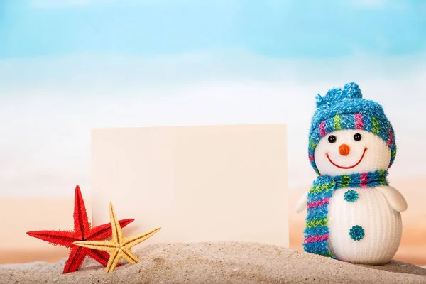 Снеговик, чистая карта и морская звезда в песке против — стоковое фото