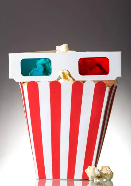 Grote vierkante doos popcorn en 3d glazen, verschillende naast grijs. — Stockfoto