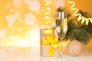 Champagne in wine glass, New Year's gift and decorated pine   branch, on yellow background