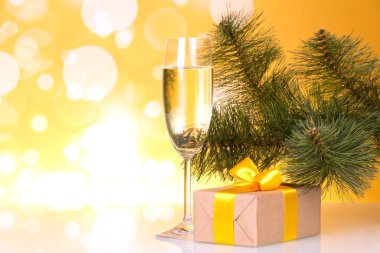 Fouger with champagne and box with gift on yellow sparkling background