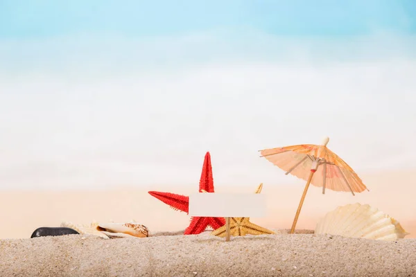 Μια λευκή κάρτα στο πάσσαλο, αστερίας, μια ομπρέλα, κέλυφος της θάλασσας — Φωτογραφία Αρχείου