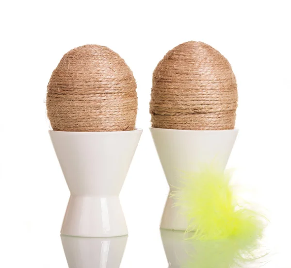 Easter eggs in cups with string entwined and feather isolated. — Stok fotoğraf