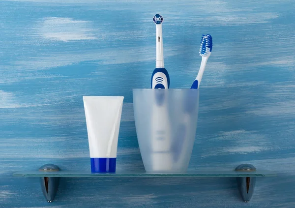 En el vaso hay cepillos y pasta de dientes al lado, en el estante, en — Foto de Stock