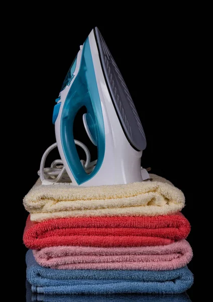 Modern electric iron stands on pile of terry towels, isolated on black — Stock Photo, Image
