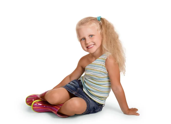 Uśmiechnięta blondynka siedząca w gumowych butach, odizolowana na biało — Zdjęcie stockowe