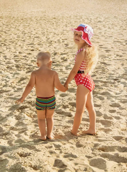 Lille pige og dreng går langs stranden, holder i hånd - Stock-foto