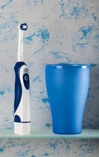 電気歯ブラシとリンス用ガラス ライトブルーの背景 — ストック写真
