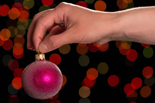Female hand holds Christmas toy for tree, on dark background — 스톡 사진