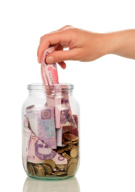 Female hand is laying money bills in glass jar, isolated 