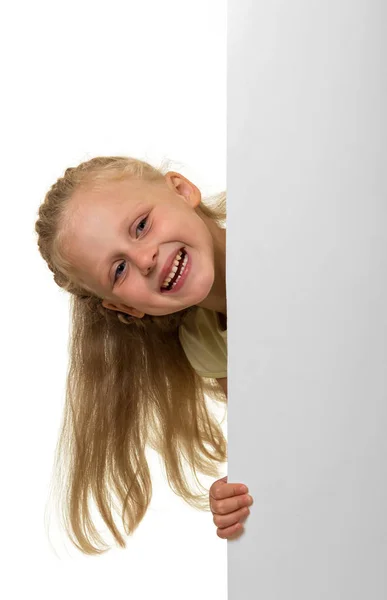 Liten blond flicka kikar ut från bakom en fana isolerad på w — Stockfoto