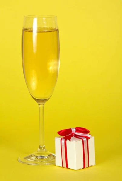 Um copo de vinho espumante e pequena lembrança decorada com fita em fundo amarelo — Fotografia de Stock