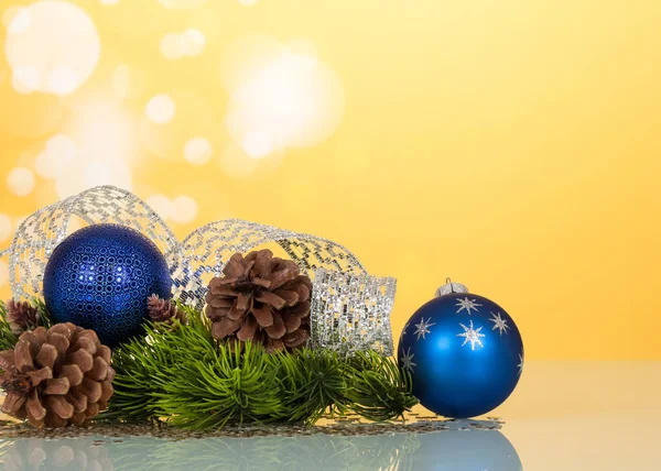 Яркие новогодние игрушки-шарики, серебряная лента и шишки, на желтом — стоковое фото