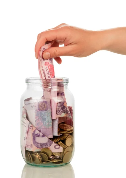 Female hand is laying money bills in glass jar, isolated — Stock Photo, Image