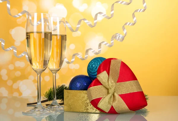 Geschenkschachtel in Herzform, Weihnachtsschmuck und Weingläser, auf gelbem Hintergrund — Stockfoto