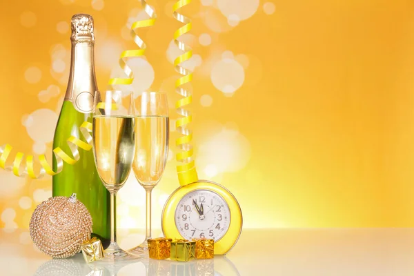 Fles champagne, glazen, kerstspeelgoed, cadeaus en klokken, op felgeel — Stockfoto